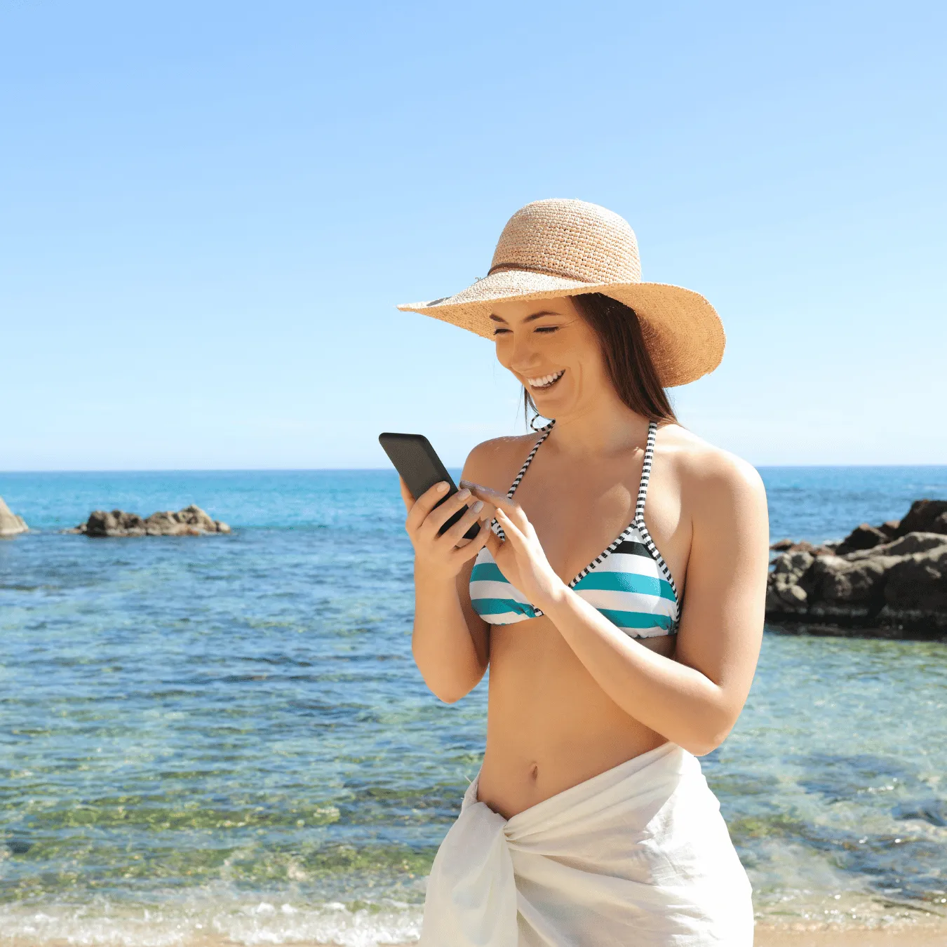 Cheerful woman at the beach holding her phone recording a video for her audience